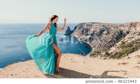 Side view a Young beautiful sensual woman with black hair in a long mint dress posing on a beach with calm sea bokeh lights on sunny day. Girl on the nature on blue sky background. Fashion photo Side view a Young beautiful sensual woman with black hair in a long mint dress posing on a beach with calm sea bokeh lights on sunny day. Girl on the nature on blue sky background. Fashion photo 96325943