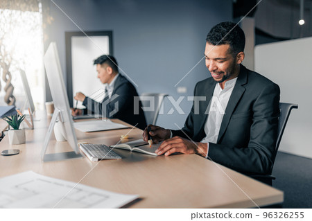 African businessman taking notes during working day in office on colleague background 96326255