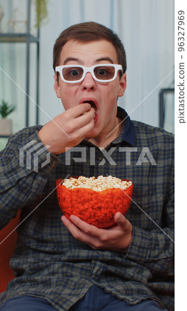 Man sitting on couch eating popcorn and watching interesting TV serial, sport game online at home 96327969