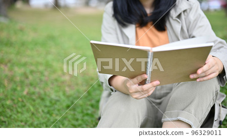 Young Asian woman enjoying reading her novel or book while relaxing in the green park Young Asian woman enjoying reading her novel or book while relaxing in the green park 96329011