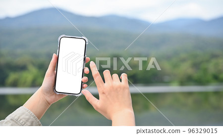 Young Asian female using her modern smartphone to take a picture of lake and mountain Young Asian female using her modern smartphone to take a picture of lake and mountain 96329015