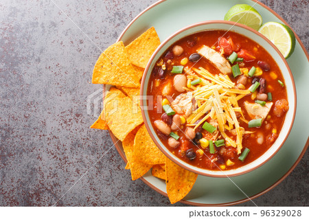 Tasty chicken taco soup full of tender chicken, sweet corn, black beans, fire-roasted tomatoes, and the most delicious creamy broth close-up in a plate. Horizontal top view Tasty chicken taco soup full of tender chicken, sweet corn, black beans, fire-roasted tomatoes, and the most delicious creamy broth close-up in a plate. Horizontal top view 96329028