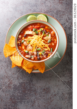 Hearty chicken taco soup packed with black beans, corn, and tomatoes with green chile peppers close-up in a plate. Vertical top view Hearty chicken taco soup packed with black beans, corn, and tomatoes with green chile peppers close-up in a plate. Vertical top view 96329029