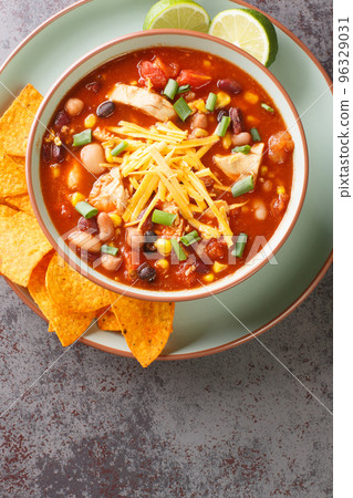 Mexican Creamy Chicken Taco Soup with black bean, corn, tomatoes, tortilla chips topped with cheddar cheese in green bowl, Vertical top view Mexican Creamy Chicken Taco Soup with black bean, corn, tomatoes, tortilla chips topped with cheddar cheese in green bowl, Vertical top view 96329031