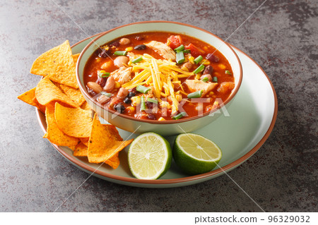 Chicken Taco Soup with black bean, corn kernels, tomatoes topped with cheddar cheese in green bowl, horizontal 96329032