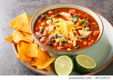 Tasty chicken taco soup full of tender chicken, sweet corn, black beans, fire-roasted tomatoes, and the most delicious creamy broth close-up in a plate. Horizontal 96329033