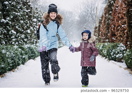 Happy Family, mother, son and cat in backpack walking on the snowy alley in winter snowy nature background. Mom, kid boy having fun, running, playing snow ball together outdoors at winter park Happy Family, mother, son and cat in backpack walking on the snowy alley in winter snowy nature background. Mom, kid boy having fun, running, playing snow ball together outdoors at winter park 96329750
