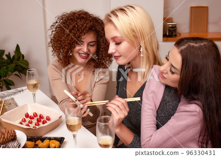 Discussing the latest gossips. Three beautiful young women talking and smiling while drinking wine and sitting on the couch together Discussing the latest gossips. Three beautiful young women talking and smiling while drinking wine and sitting on the couch together 96330431