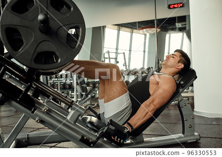 Young man is engaged on a modern simulator in the gym. Male athlete is doing exercises for legs with training machine. Young man is engaged on a modern simulator in the gym. Male athlete is doing exercises for legs with training machine. 96330553