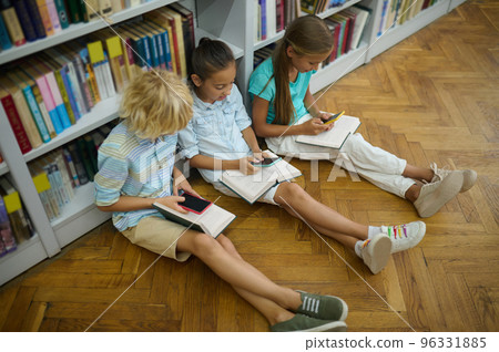 Group of kids reading while sitting on the floor in the library Group of kids reading while sitting on the floor in the library 96331885