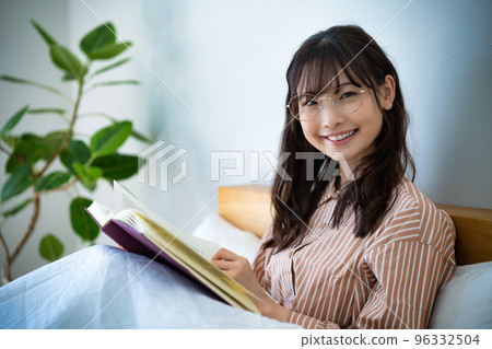 戴眼鏡在床上看書的年輕女子 96332504