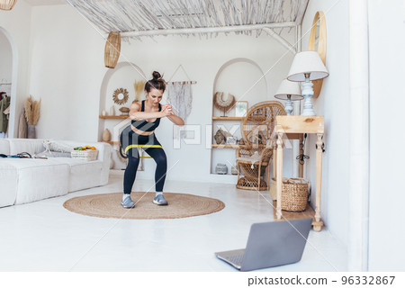 Woman working out at home doing squats with elastic band. 96332867