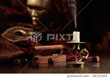 Extinguished candle, dice, and carnival masks on an old wooden table. 96332905