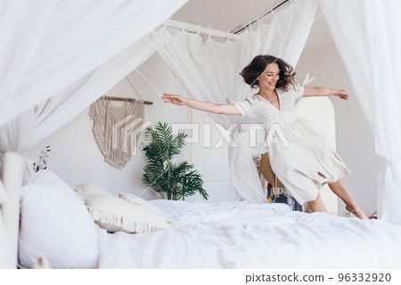 Young woman jumps on the bed Young woman jumps on the bed 96332920
