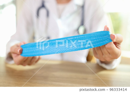 Physical therapist with medical tape in hands sitting at desk in clinic. Physical therapist with medical tape in hands sitting at desk in clinic. 96333414