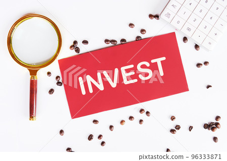 Invest word on a red card with scattered coffee beans on the table and a magnifying glass as a symbol reminding you to focus when choosing an investment Invest word on a red card with scattered coffee beans on the table and a magnifying glass as a symbol reminding you to focus when choosing an investment 96333871