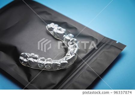 close-up, invisible plastic braces on a black special zip package, lying on a blue background. studio shot, dental clinic background close-up, invisible plastic braces on a black special zip package, lying on a blue background. studio shot, dental clinic background 96337874