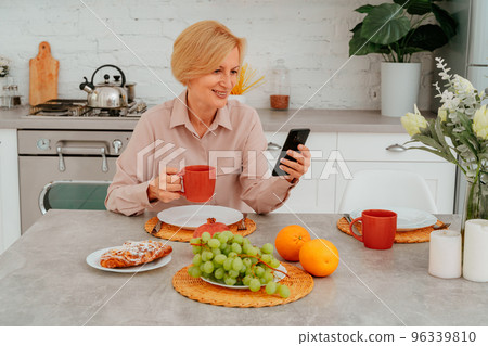Woman has breakfast at home with fruits,cake and coffee and reads news from smartphone 96339810