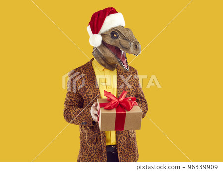 Funny man in dinosaur mask, Christmas hat and leopard jacket holding Christmas gift 96339909