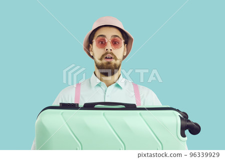 Young traveler holding his suitcase and looking at camera with funny surprised face expression 96339929