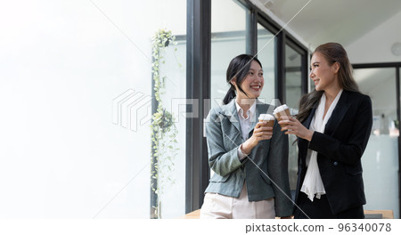 Diverse employees chatting during coffee break, walking in modern office, Asian businesswoman wearing glasses sharing ideas, discussing project with colleague, having pleasant conversation 96340078