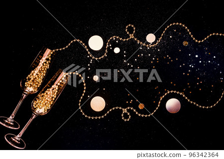 Glasses of champagne and golden shiny holiday decor, balloons on black background with sparkles 96342364