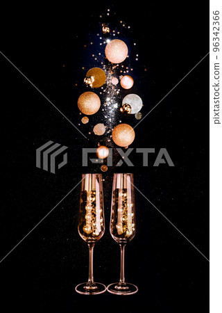 Glasses of champagne and golden shiny holiday decor, balloons on black background with sparkles 96342366