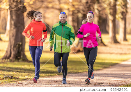 A trio of runners, two young women and one mature man are running in an autumn park 96342491
