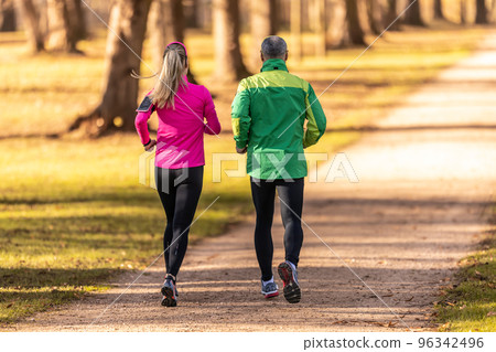 Rear view of a two runners, young woman and one mature man running in an autumn park 96342496
