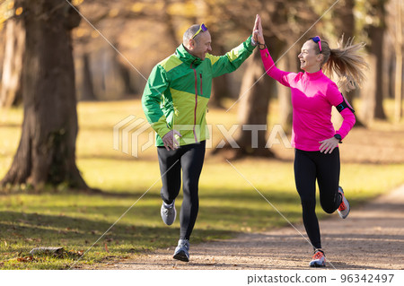Two runners mature man and young woman support each other and give high-five while a run Two runners mature man and young woman support each other and give high-five while a run 96342497