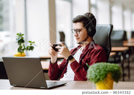 Creative man looking at screen typing message with smartphone. Young man relaxing using laptop. Creative man looking at screen typing message with smartphone. Young man relaxing using laptop. 96343382