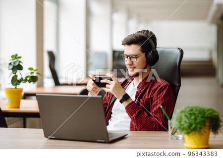 Creative man looking at screen typing message with smartphone. Young man relaxing using laptop. Creative man looking at screen typing message with smartphone. Young man relaxing using laptop. 96343383