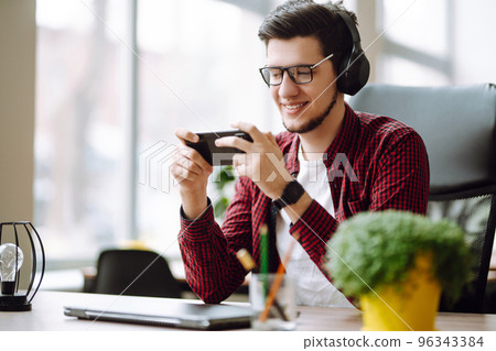 Creative man looking at screen typing message with smartphone. Young man relaxing using laptop. Creative man looking at screen typing message with smartphone. Young man relaxing using laptop. 96343384