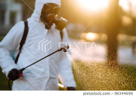Man wearing protective suit disinfecting public places in the sun with spray chemicals. Covid -19. 96344699