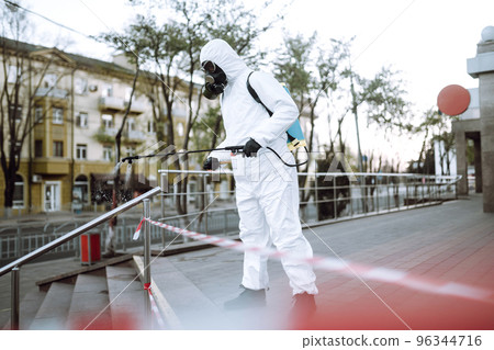 Man in protective suit and mask sprays disinfector onto the railing in the public place. Covid -19. Man in protective suit and mask sprays disinfector onto the railing in the public place. Covid -19. 96344716