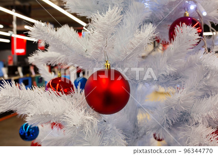 Red Christmas ball on a white Christmas tree in the mall. Christmas time. New year eve. Winter holidays. Red Christmas ball on a white Christmas tree in the mall. Christmas time. New year eve. Winter holidays. 96344770