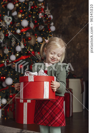 Little happy smiling girl with Christmas gift box on xmas tree background. Traditional xmas present. Vertical frame Little happy smiling girl with Christmas gift box on xmas tree background. Traditional xmas present. Vertical frame 96345810