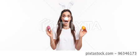 Easter party begins. Portrait of funny and cute, silly young caucasian woman celebrating divine day, wear rabbit ears and nose, holding colored eggs, gasping amused, white background 96346173