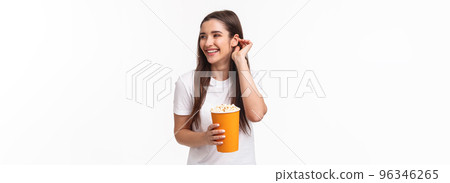 Entertainment, fun and holidays concept. Portrait of beautiful young carefree friendly woman in glasses, place hair strand behind ear giggle joyful watching movie in cinema, eating popcorn 96346265