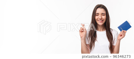 Travelling, holidays, summer concept. Journey beggings. Happy cheerful brunette girl in t-shirt, close eyes and smiling, making wish, cross fingers good luck, holding passport with plane ticket Travelling, holidays, summer concept. Journey beggings. Happy cheerful brunette girl in t-shirt, close eyes and smiling, making wish, cross fingers good luck, holding passport with plane ticket 96346273