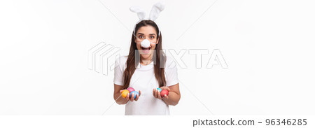 Portrait of excited, happy and carefree young woman spending holiday with family, wearing funny rabbit ears and nose, holding colored eggs, painting it with kids on Easter day, white background 96346285