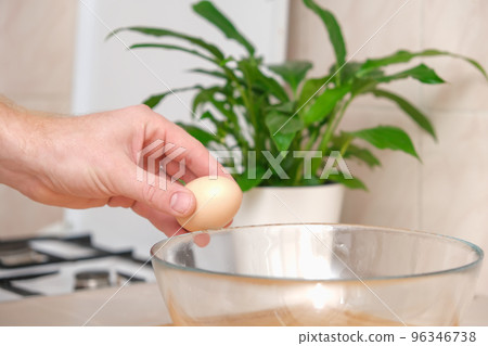 A man breaks a chicken egg on the edge of a 96346738