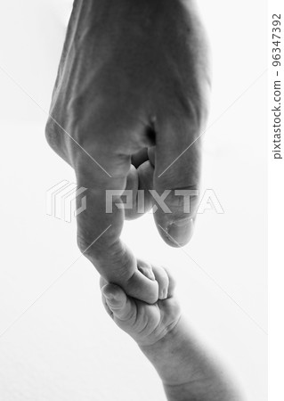 Close-up little hand of child and palm of mother and father. The newborn baby has a firm grip on the parent's finger after birth. A newborn holds on to mom's, dad's finger. Black and white photo. Close-up little hand of child and palm of mother and father. The newborn baby has a firm grip on the parent's finger after birth. A newborn holds on to mom's, dad's finger. Black and white photo. 96347392