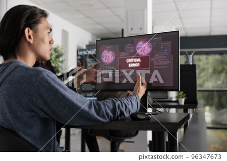 Nervous app developer having system error message on computer screen, trying to solve hacking alert problem. System engineer looking at hacked server on pc monitor in it office room. Nervous app developer having system error message on computer screen, trying to solve hacking alert problem. System engineer looking at hacked server on pc monitor in it office room. 96347673
