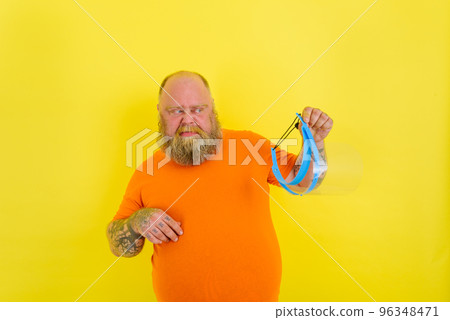 Doubter man with beard and tattoos is worried about a protective face shield against covid-19 96348471