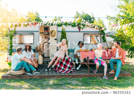 Friends have a picnic with a camper in a green meadow Friends have a picnic with a camper in a green meadow 96350161