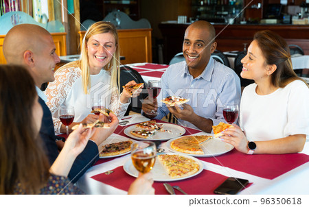 Cheerful friends enjoying dinner with pizza in cozy restaurant 96350618