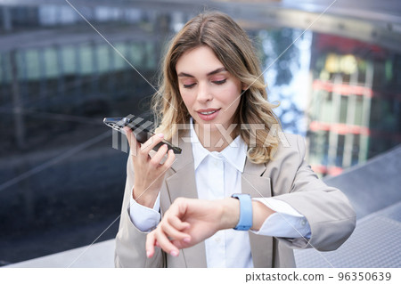 Businesswoman checks time on digital watch and records voice message, arranges a meeting, sits outside in city centre Businesswoman checks time on digital watch and records voice message, arranges a meeting, sits outside in city centre 96350639