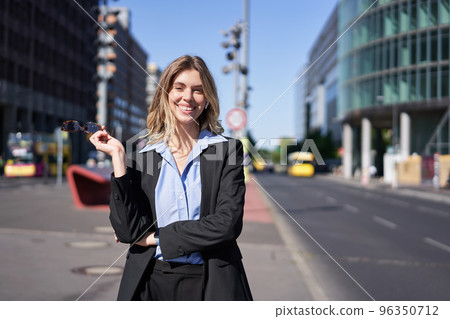 Portrait of successful young company ceo, businesswoman in black suit, standing on sunny street and smiling 96350712