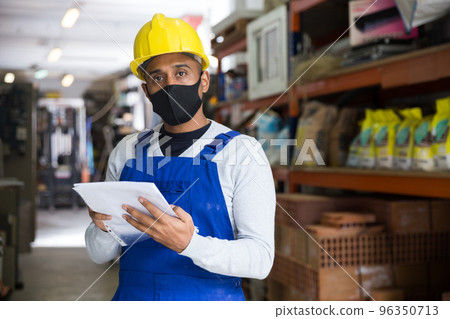 Warehouse worker in protective mask making notes during inventory of building materials 96350713